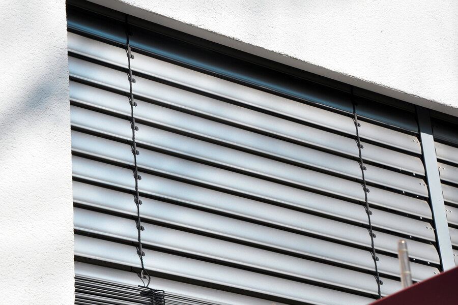 Detailaufnahme der aluminiumfarbenden Lamellen einer Außenjalousie heruntergelassen vor einer Terrassentür