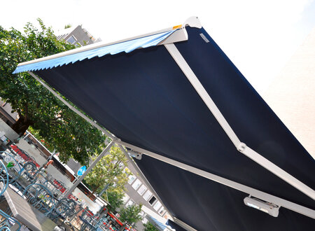 Doppelmarkise in blau mit weißen Metallstützen über den Außensitzplätzen eines Cafés ausgerüstet mit Unterbauheizstrahlern 
