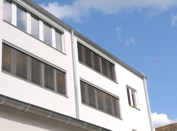 Fassade eines öffentlichen Gebäudes mit Außenjalousien vor den Fenstern, teilweise herunter gelassen.