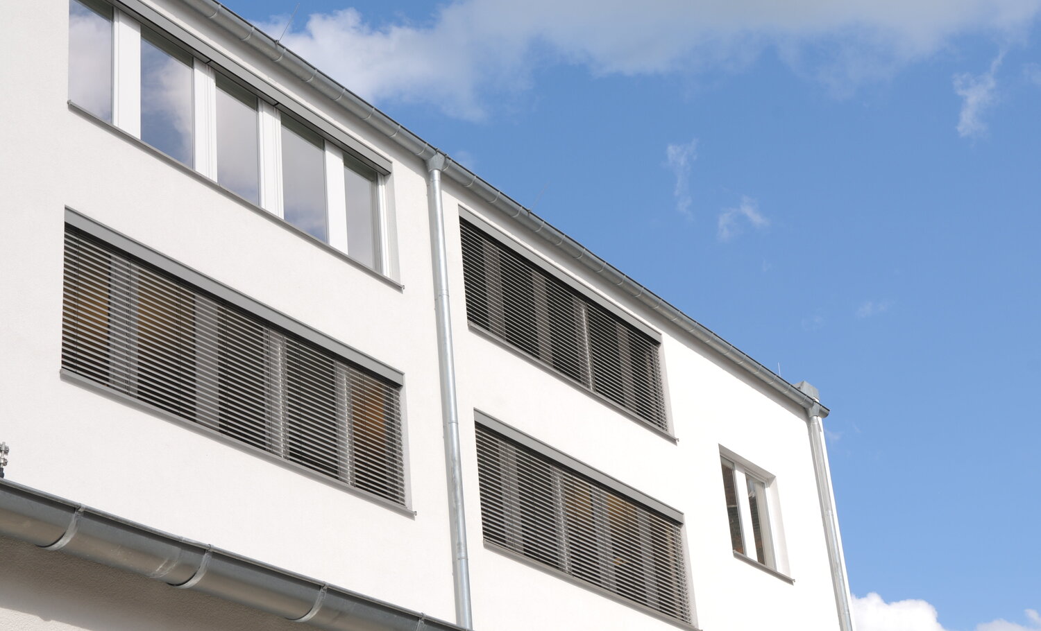 Ansicht eines Bürohauses mit Außenjalousien, teils ganz heruntergelassen – an einem Fenster hochgefahren