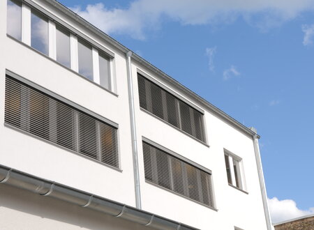 Fassade eines öffentlichen Gebäudes mit Außenjalousien vor den Fenstern, teilweise herunter gelassen.