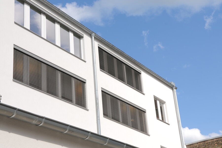 Fassade eines öffentlichen Gebäudes mit Außenjalousien vor den Fenstern, teilweise herunter gelassen.
