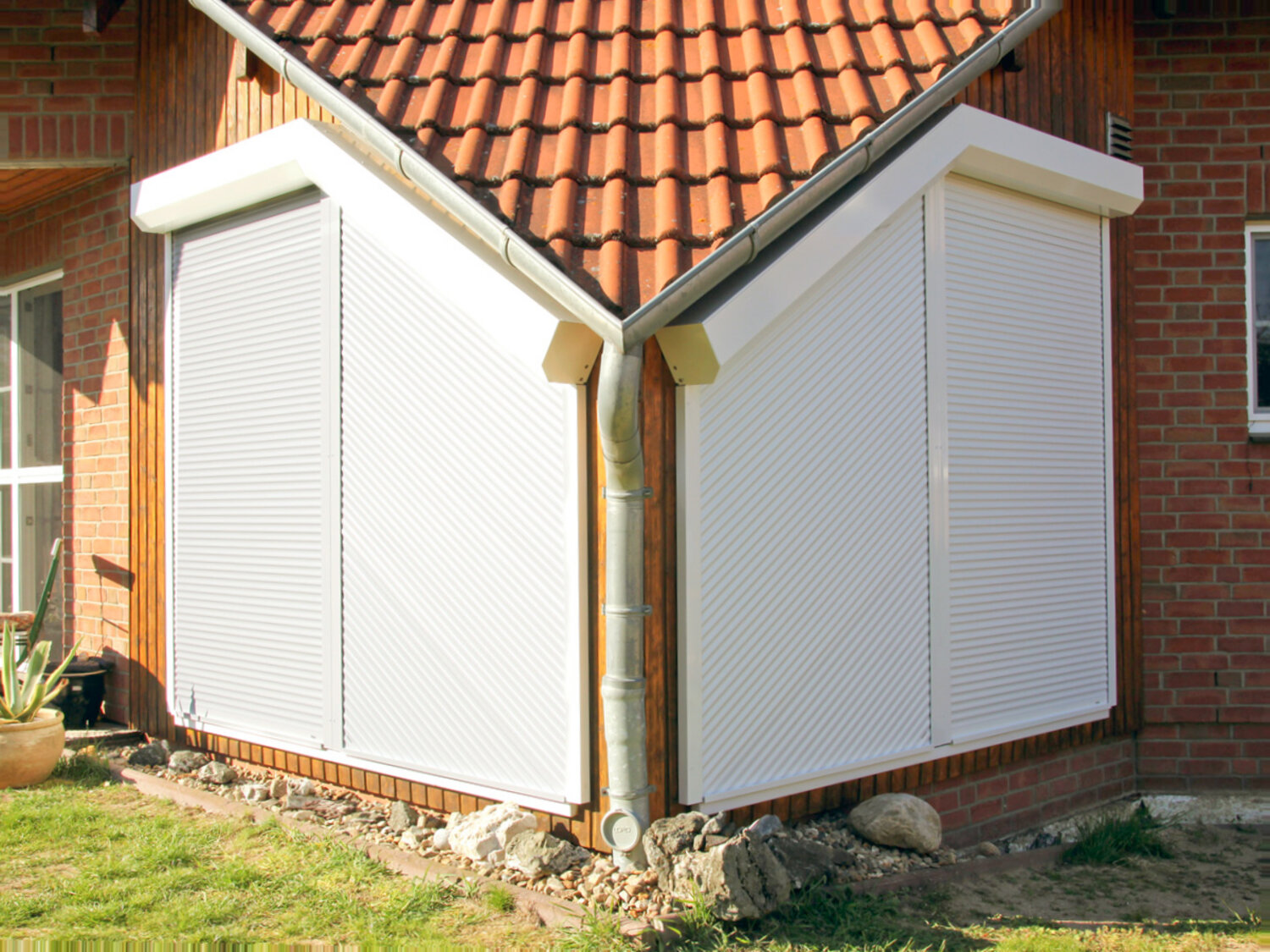 Herabgelassene Schrägrollläden vor einer mehrteiligen Fensterfront im Dachgeschoß eines Wohngebäudes