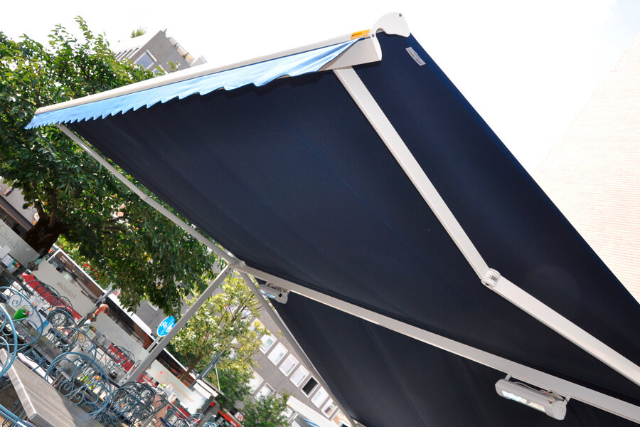 Doppelmarkise in blau mit weißen Metallstützen über den Außensitzplätzen eines Cafés ausgerüstet mit Unterbauheizstrahlern 