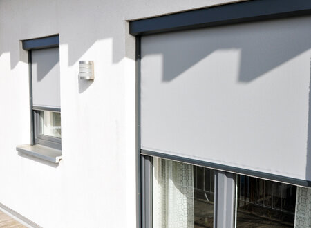 Maßgefertigte Zip Screen Anlage in grau mit blickduchlässigem Sonnenschutz für Fenster und Türen an einem Wohnhaus