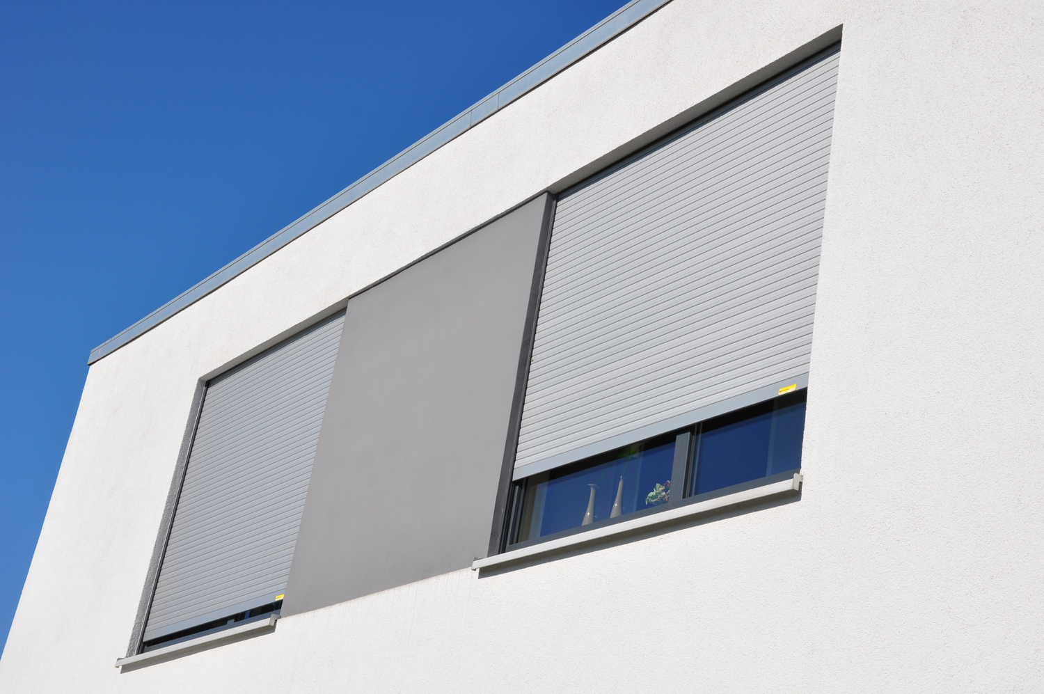Außenansicht zweier Fenster eines Bürohauses mit heruntergelassenen Rollläden in lichtgrau