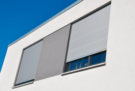 Außenansicht zweier Fenster eines Bürohauses mit heruntergelassenen Rollläden in lichtgrau