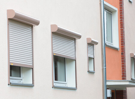 Vorbaurollläden mit rundem, aluminiumfarbendem Rollladenkasten vor Fenstern einer Wohnanlage