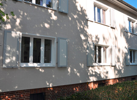 Klappläden in lichtgrau, offen und geschlossen vor den Fenstern eines Wohnhauses