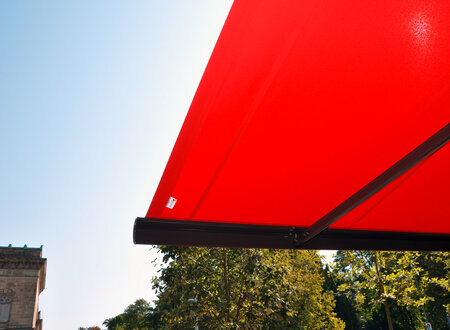 Großflächige Ladenmarkise – mit Detailansichten - in rot als Sonnenschutz für die Außensitzplätze eines Restaurants