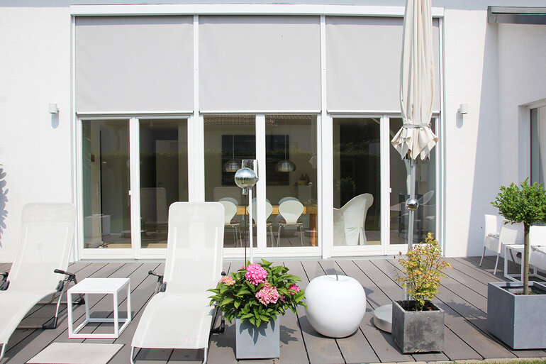 Blick auf die Terrasse mit halb heruntergelassene Zip-Screen Anlagen in lichtgrau an einer Terrassen-Fensterfront