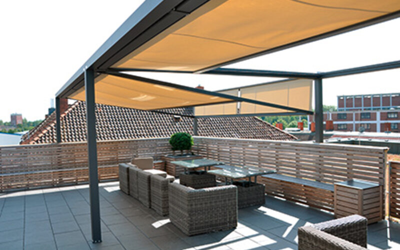 Das freistehende Beschattungssystem Q,Bus auf einer Dachterrasse mit schwarzer Metallkonstruktion und Markisen in beige.