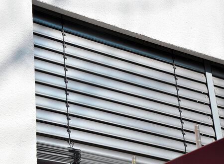 Detailaufnahme der aluminiumfarbenden Lamellen einer Außenjalousie heruntergelassen vor einer Terrassentür