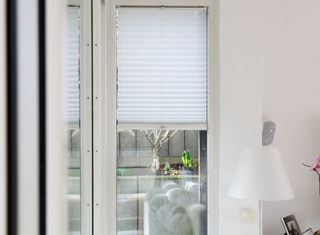 Weißes Plisee vor Fenster eines Wohnhauses halbhochgezogen